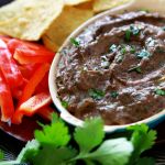 black bean hummus in a bowl surrounded by tortilla chips and other vegetables to dip